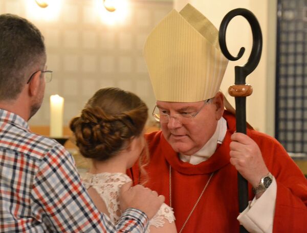 Weihbischof Bongartz firmt ein Mädchen, der Pate legt die Hand auf ihre Schulter