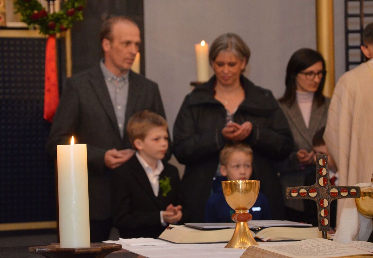 Familien feiern Erstkommunion, auf dem Altar stehen Kelch und Kreuz