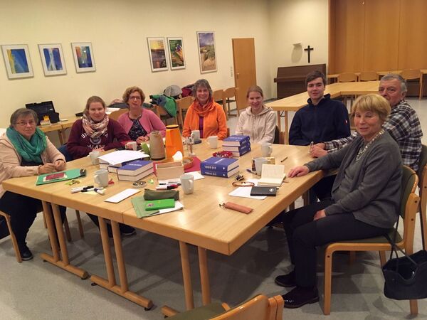 Mitglieder des Kirchort-Team sitzen am Tisch, auf dem Tisch sind Teetassen, Bibeln, Zettel, Stifte, Schokolade
