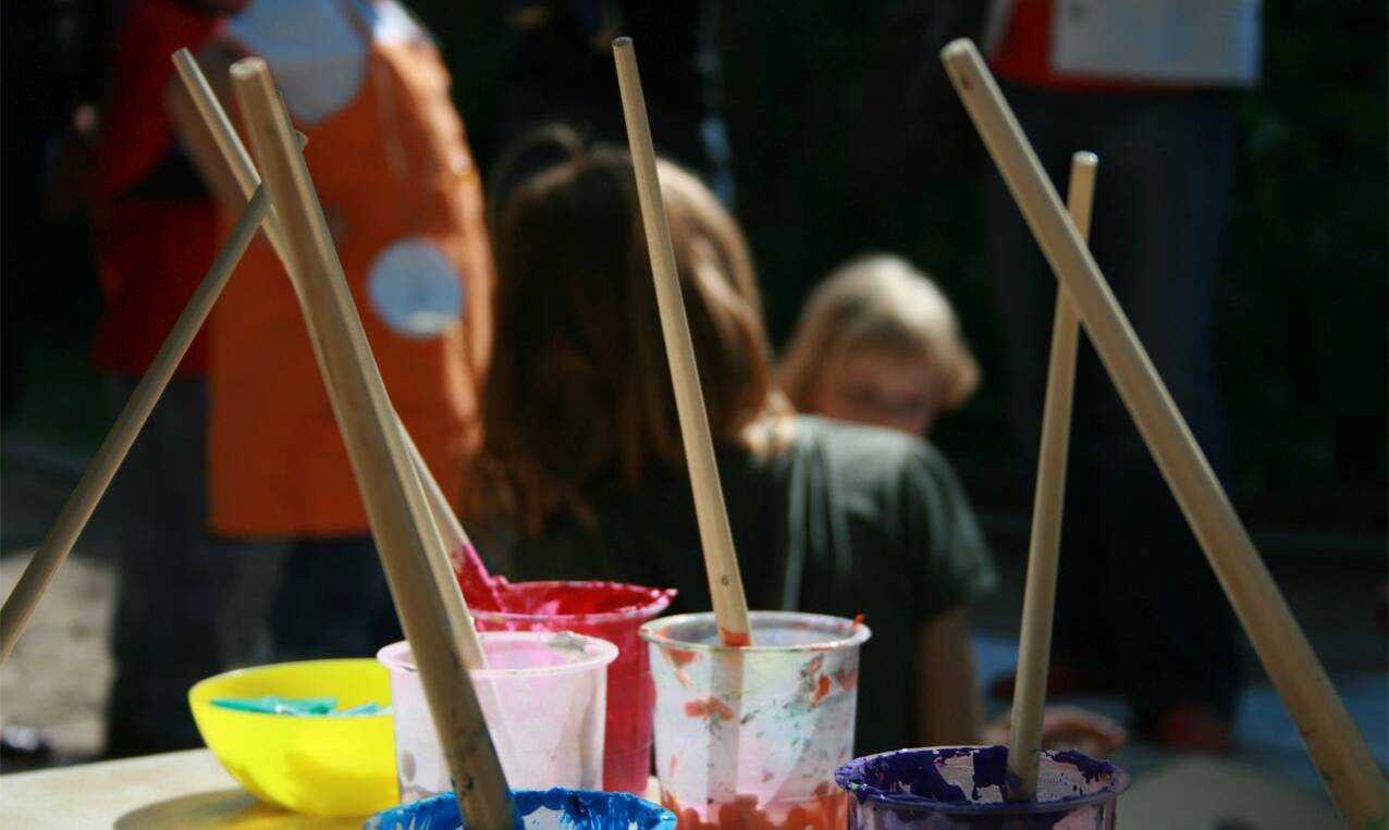 Malfarben und Pinsel, im Hintergrund Kinder