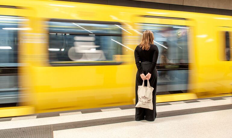 Ein Frau steht still auf dem Bahnsteig, hinter fährt ein Zug vorbei