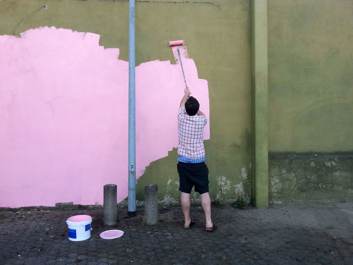 jemand streicht eine dunkle Hauswand mit rosa Farbe