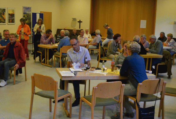 Menschen sitzen an Tischen im Pfarrsaal in Sarstedt
